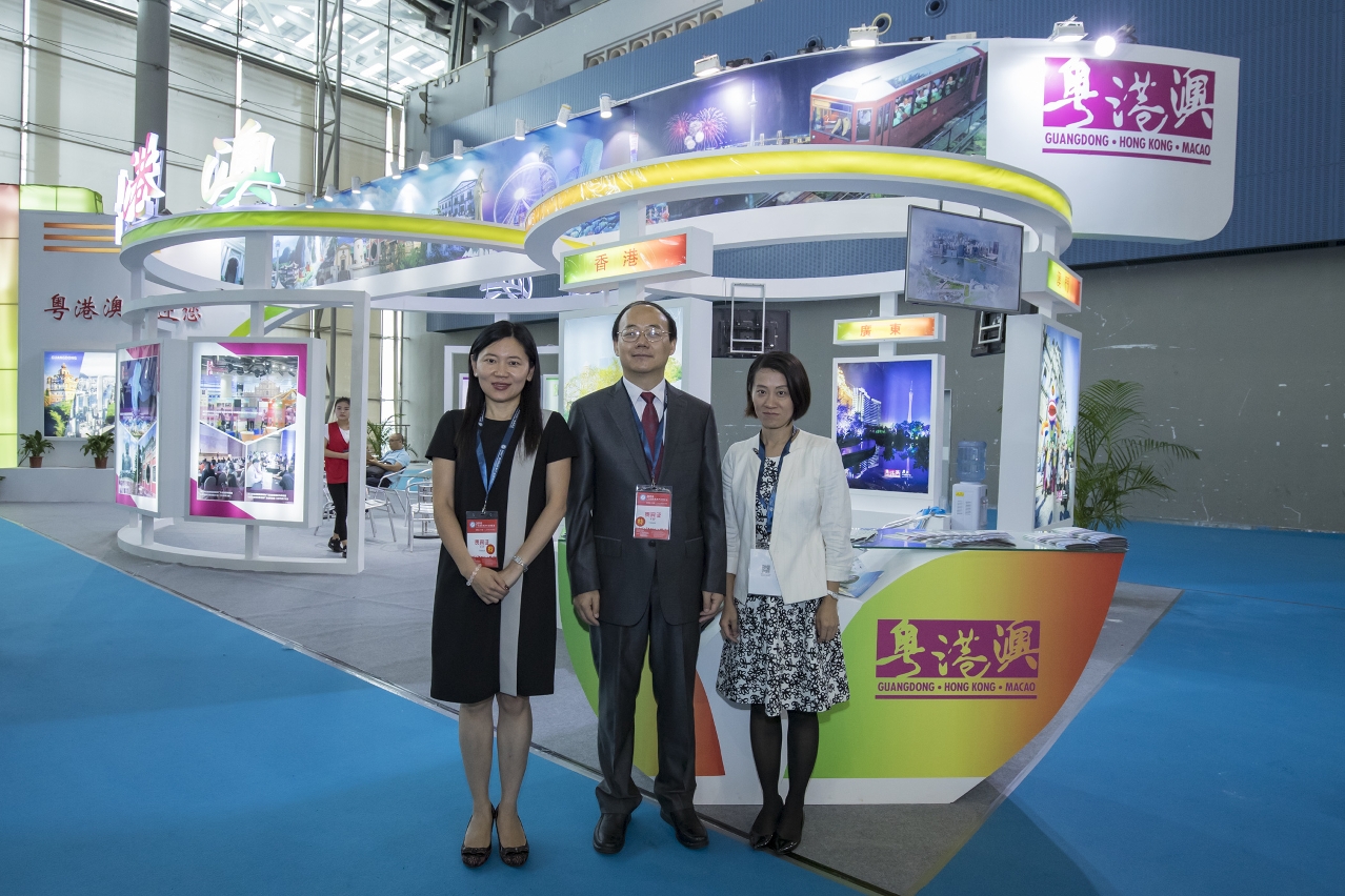 O subdirector da Administração do Turismo de Guangdong, Mei Qijie (no meio), a subdirectora da DST, Cecilia Tse (à esq.), e uma representante do HKTB (à dta.), em frente ao expositor conjunto de Guangdong, Hong Kong e Macau