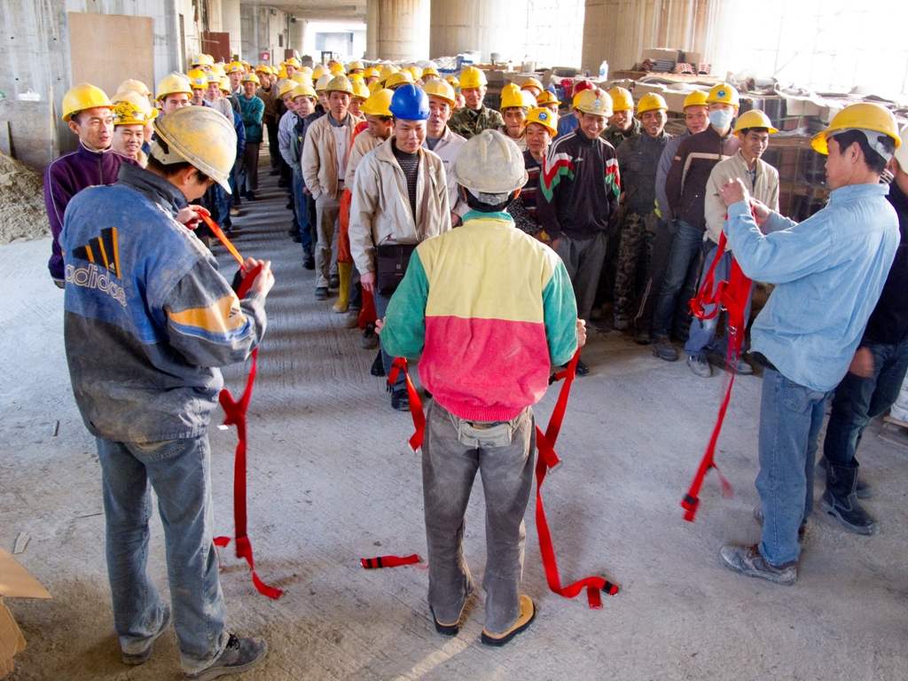 O encarregado de segurança do estaleiro mostra aos trabalhadores os aspectos principais de segurança no trabalho e faz a demonstração da utilização do cinto de segurança durante as “instruções de segurança matinais”.